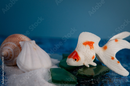 A plastic goldfish with white sand and seashells