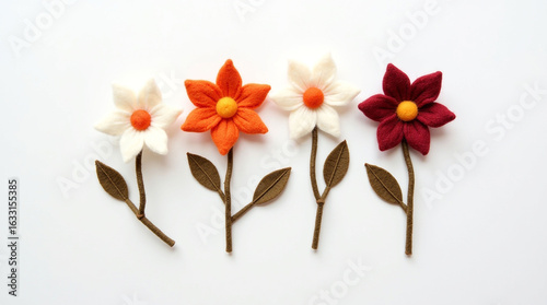 A collection of minimalist, handcrafted felt or yarn flowers and leaves arranged neatly on a clean white background