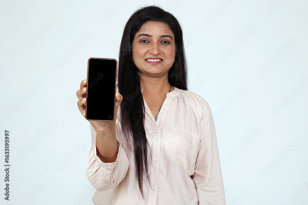 Beautiful indian woman showing mobile phone looking in front of the camera wearing casual light pink shirt isolated over studio background. Beautiful indian woman showing mobile phone looking in front of the camera wearing casual light pink shirt isolated over studio background.