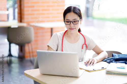 Asian young female medical student in casual cloth doing homework with laptop  in collage with sun bright background. Asian school concept.