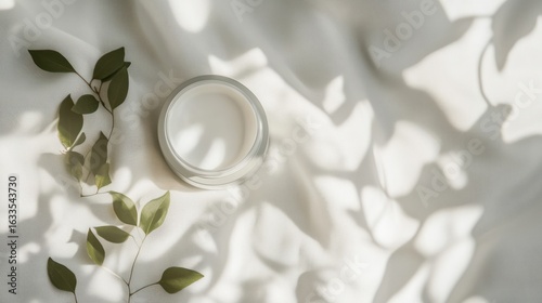 White cosmetic jar, soft fabric, and leaves