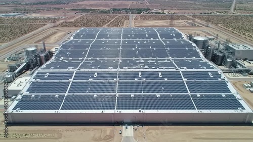 Aerial view of a large industrial building covered in solar panels in a desert landscape setting
