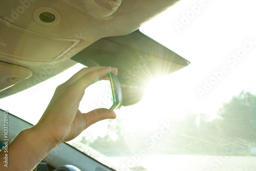 Female hand adjusting rearview mirror in car against sunlight through windshield