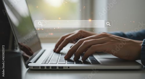 Closeup of hands typing on a laptop keyboard with a search bar interface visible, representing online research and information gathering
