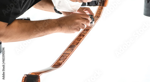 A man closely examining a developed color film strip under magnification on a white background.