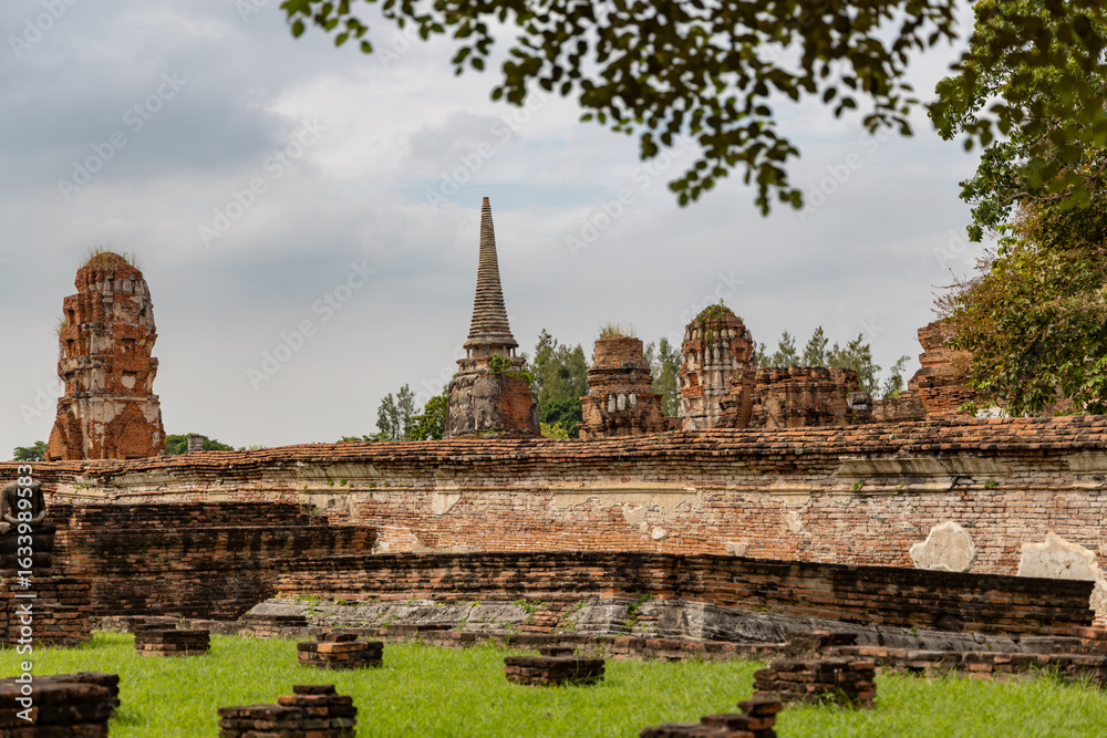 Fototapeta premium Ancient temple ruins and brick wall structures in Ayutthaya Historical Park, Thailand