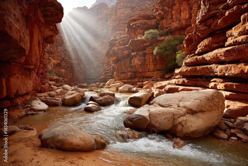 Sunbeams illuminate a narrow canyon, flowing river, and large rocks