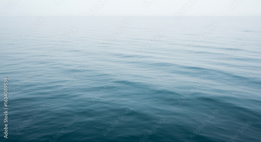 Obraz premium Calm, serene ocean surface fading into a misty, overcast sky.