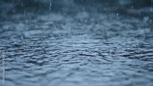 Detailed close up of heavy rain falling onto a tranquil water surface creating mesmerizing ripples and splashes perfect for a calming or nature background video