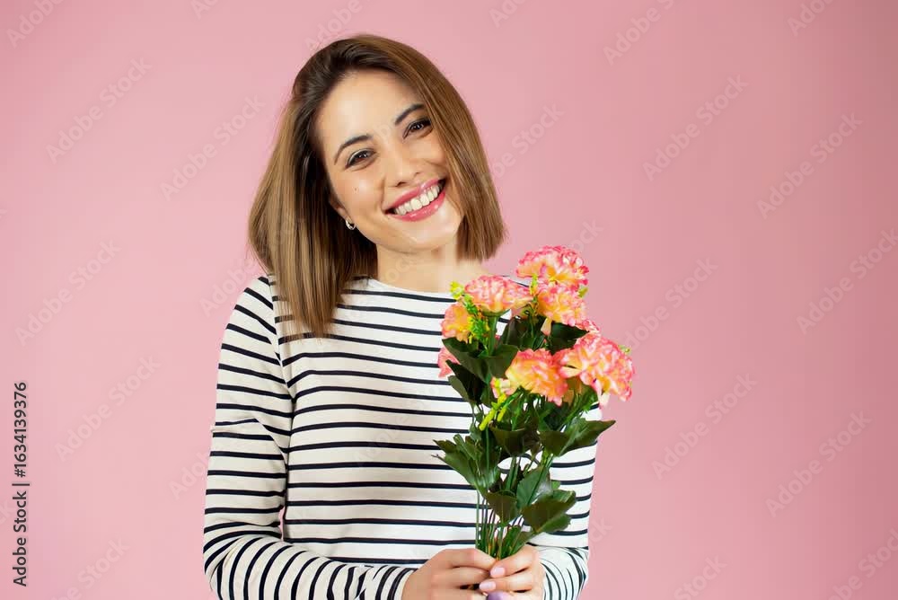 Young smiling woman wearing striped shirt holding bouquet of flowers isolated over pink background. Young smiling woman wearing striped shirt holding bouquet of flowers isolated over pink background.