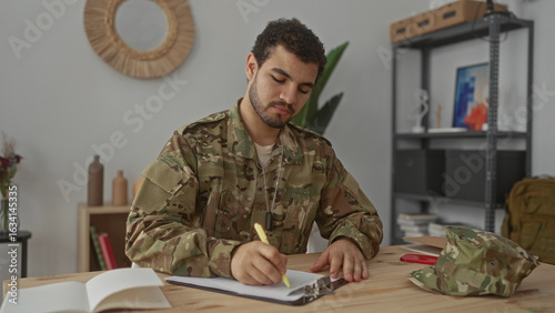 Konstfotografi Man writing on clipboard with right hand at desk in military building interior wearing camouflage uniform and dog tags; duty