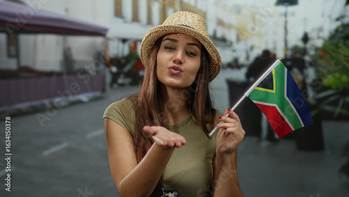 Foto Woman smiling and blowing a kiss with south african flag on an outdoor street wh