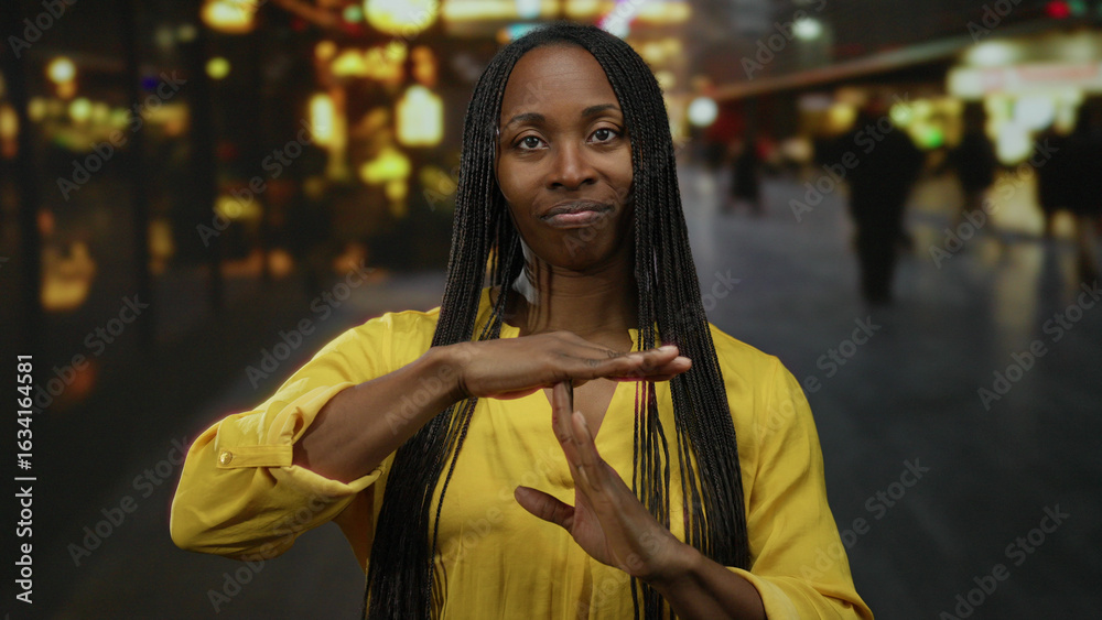 Φωτογραφία Woman gesturing on an urban street at night wearing a yellow shirt with braids visible in a city setting, conveying time concept outdoors in a lively environment
