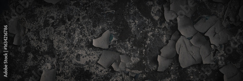 Dark wide panoramic background. Peeling paint on a concrete wall. Dark grunge texture of old cracked flaking paint. Weathered rough painted surface. Patterns of cracks. Darkness background for design.