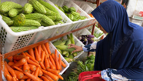 Muslim women wearing hijab are shopping for vegetables at a shop stall