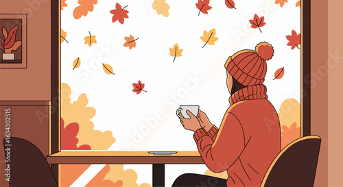 A person in a red sweater enjoys a hot drink while watching autumn leaves fall outside a large window.