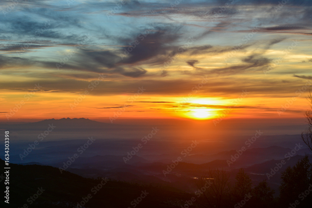 Obraz premium Vibrant sunrise in shades of gold, orange, and fiery red over a vast, expansive landscape in a warm, ethereal glow. Concepts of new beginnings, hope, awakening, tranquility, and the profound beauty