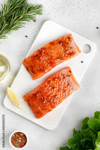 Marinated Salmon with sauce, red marinade, spicy. Fish steaks, slices. Raw uncooked salmon fillet fish with rosemary, lemon and pepper on white cutting board and grey background.