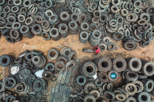 Bogura, Bangladesh - 12 April 2022: Aerial view of countless tires scattered across the ground, a stark landscape punctuated by the bright red of a lone figure amidst the rubbery chaos.