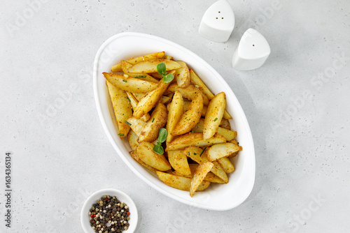 Baked potato wedges in white baking dish. Roasted potatoes with herbs and spices. Top view with copy space.