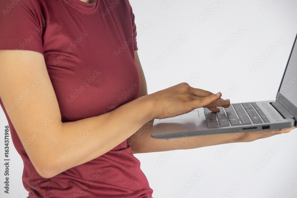Naklejka premium A focused shot captures a person in a deep red top, expertly navigating a sleek silver laptop.