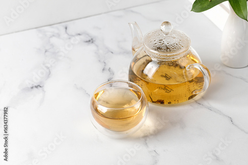 Double Wall Glass Cup with green tea and glass teapot on white marble background