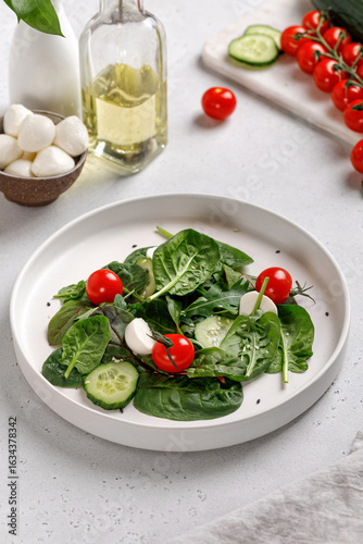 Green vegetables Salad with mix salad leaves, spinach, tomatoes and mozzarella on white plate.