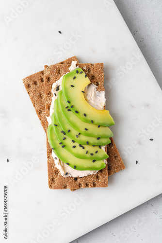 Green organic avocado slices on cream cheese on bread with black sesame seeds. Marble board