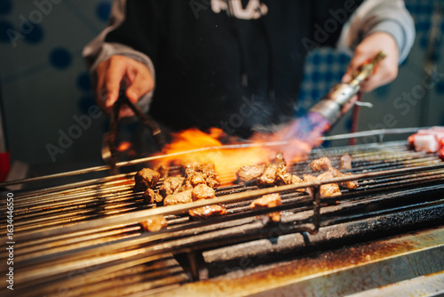 Canvas Print A chef uses a torch to sear marinated meat skewers on a grill