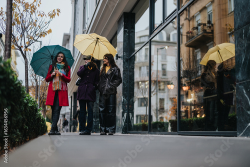 Three friends stroll together on a rainy day, carrying vibrant umbrellas and enjoying the urban scenery.