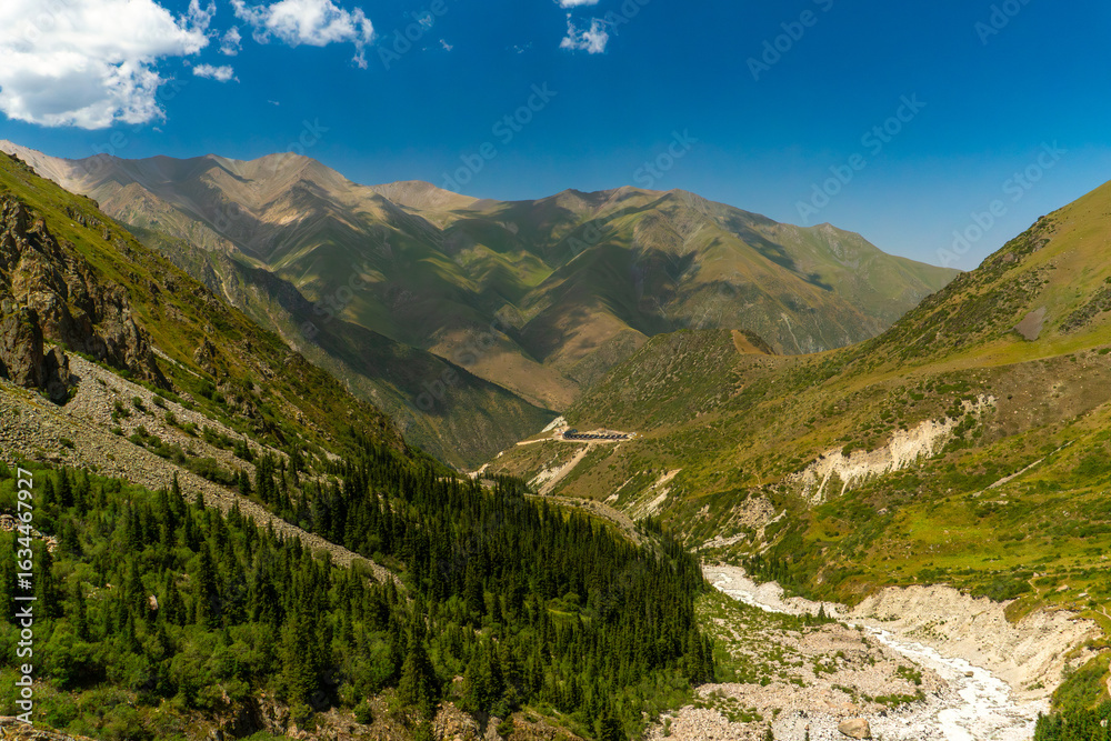 Naklejka premium Ala-Archa Mountain camp. Steep slopes, alpine meadows, coniferous forest, rocky riverbed. Distant summits ideal for hiking, mountaineering, backpacking, daytrips and wilderness adventure experiences