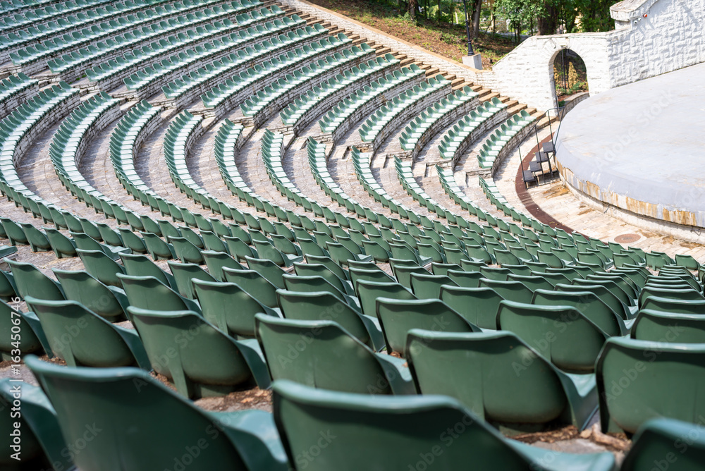 Fototapeta premium Large, open-air stone amphitheater is filled with numerous rows of green plastic seats arranged in a semi-circular pattern