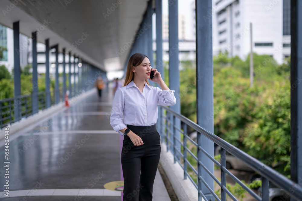 Fototapeta premium Businesswoman walking and talking on phone in modern city walkway