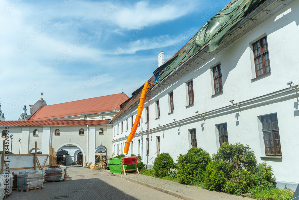 Obraz premium Historic buildings require careful renovation, building debris travels through an orange chute during roof repairs. Renovation of an old building. The roof is under construction.