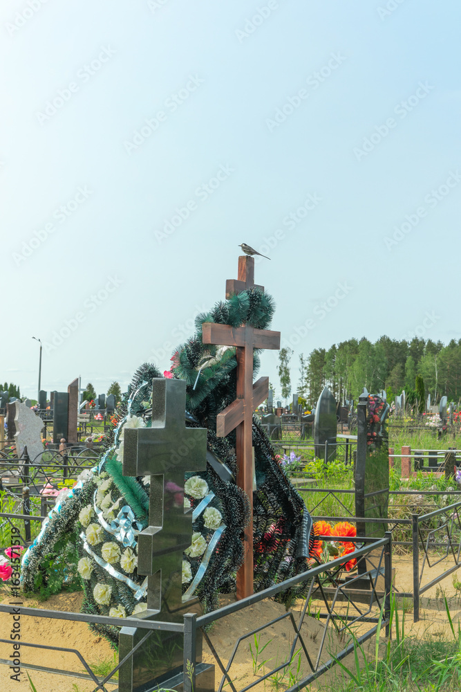 Fototapeta premium A tranquil wagtail perched on a memorial cross symbolizing hope and remembrance surrounded by vibrant flowers reflecting the beauty of life. Flowers on a grave.