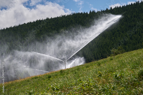 Fotografie Agricultural sprinkler system irrigating alpine meadow on mountain slope