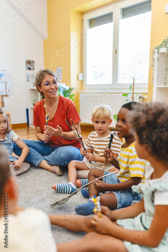 Preschool teacher leading a fun interactive activity with children sitting in a circle, raising hands and smiling in a bright classroom