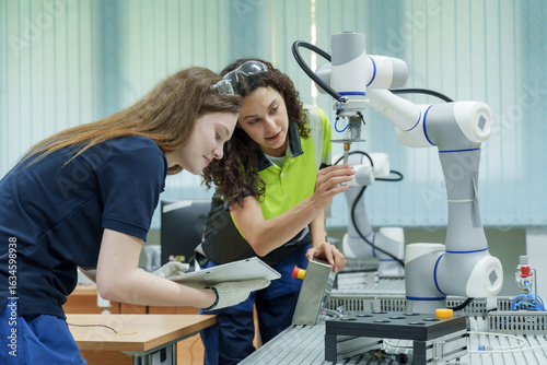 multiracial female trainees collaborate in automation lab with robotic arm and tablet to perform hands on machine training and real world smart factory skill development