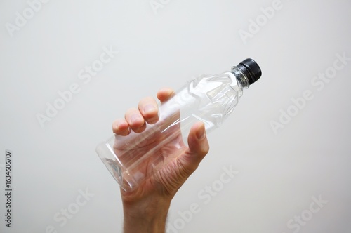 caucasian hand holding an empty transparent plastic bottle of water on white background