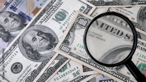 hand with magnifying glass checking 100 USA dollar banknote on money background, exchange money
