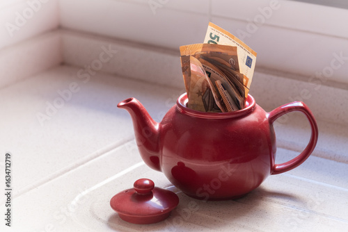 Tableau sur toile Euro banknotes hidden inside red teapot on kitchen counter