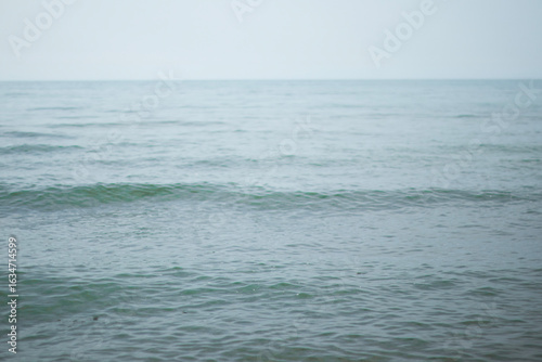 Foto Open water scene with long, even ripples crossing a pale blue-green surface under hazy sky