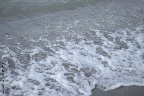 Фотография Tight view of a small shore-break washing over wet beige sand