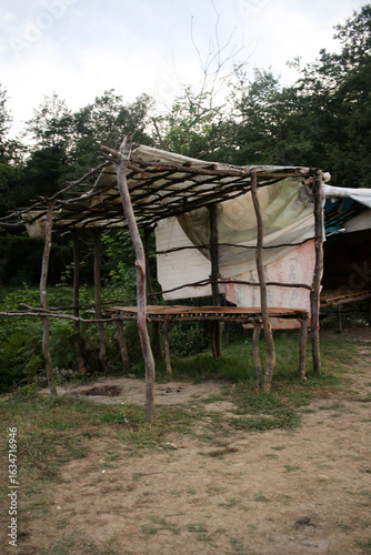 Fotografía Rustic open shelter built from uneven wooden poles and a simple overhead lattice, partially covered with fabric