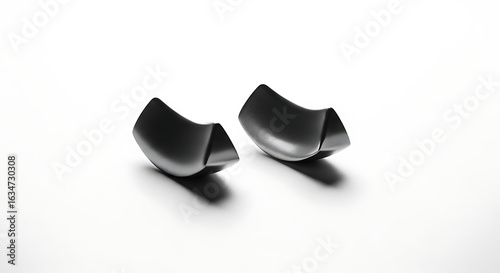 Two dark gray curved objects with triangular cutouts on a white surface casting soft shadows beneath them ai generated