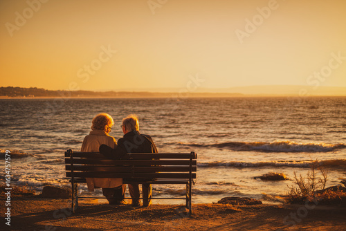 Middle-aged couple sitting on a bench by the sea during an autumn sunset