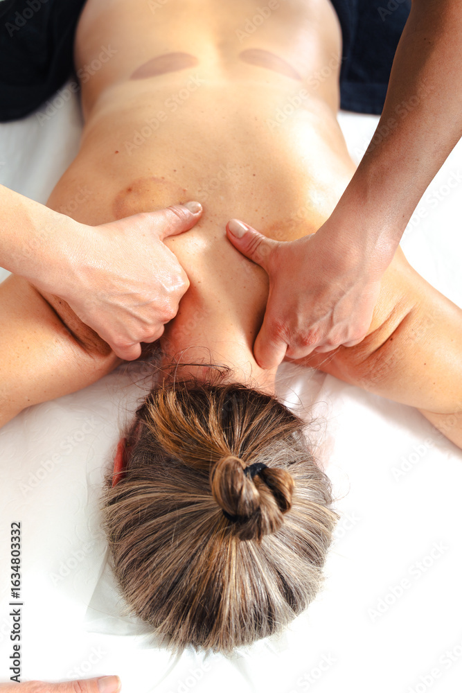 Naklejka premium Close up of therapist hands applying firm pressure along the client is upper back muscles on a white massage table, focusing on muscle relaxation, tactile care, therapeutic spa treatment indoors 