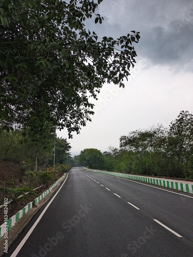 Image of the road from Thotlakonda Stupa to Beach, down the hill, with view of clean road, sea, clouds and vegetation, in the Vizag city of Andhra Pradesh. It shows the coastal area of Bay of Bengal.