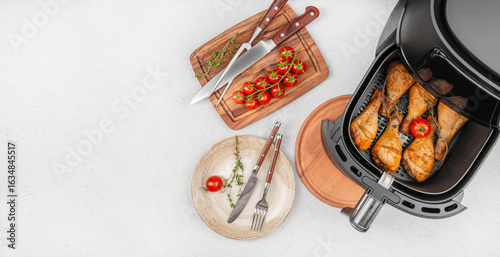 Bild auf Leinwand Air fryer chicken drumsticks with fresh tomatoes and herbs on a modern kitchen countertop
