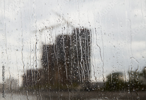 Tableau sur toile Blurred shot of water streaks on glass with monochrome silhouettes of building and crane outside window
